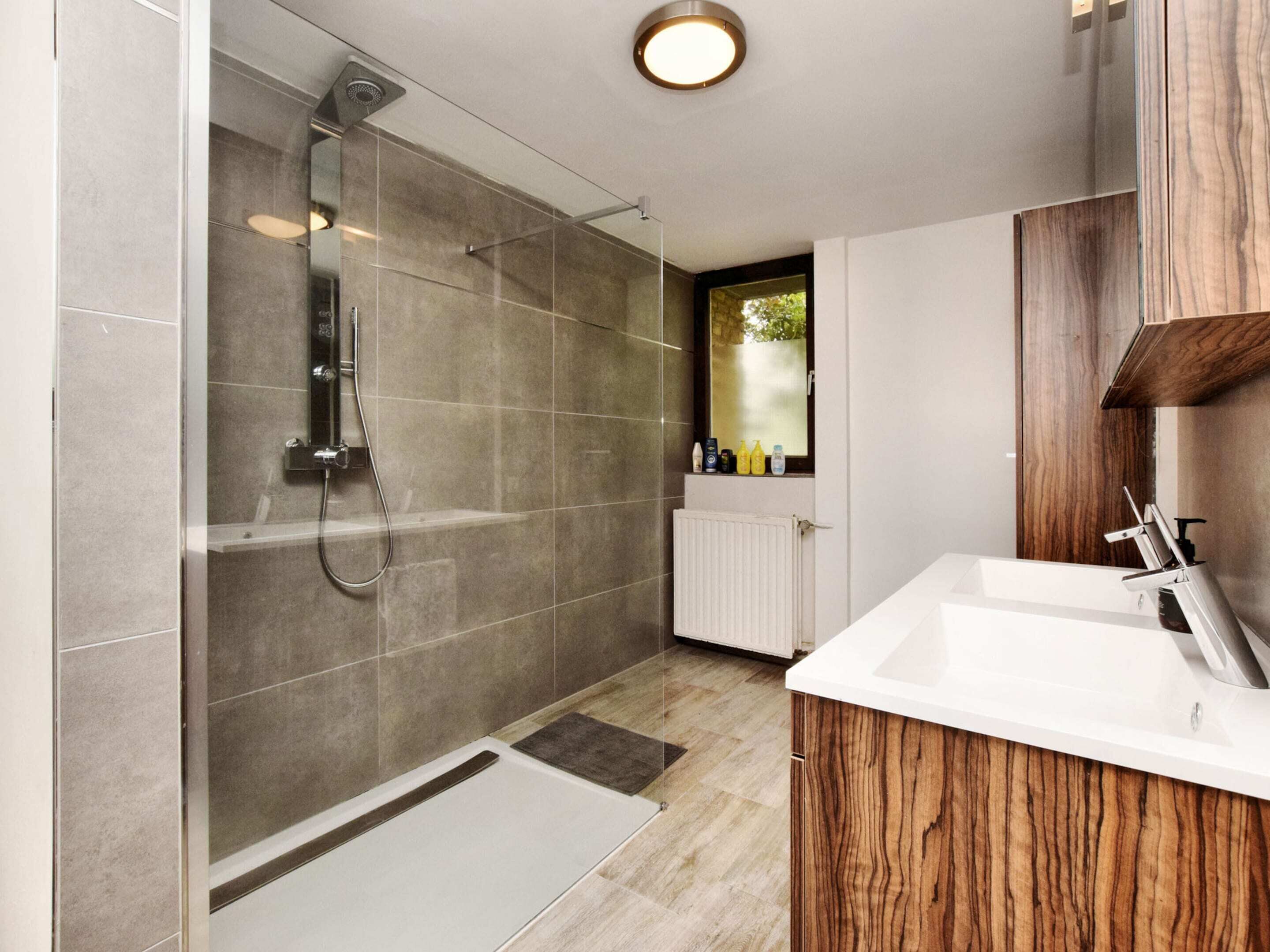 A modern bathroom with a glass-enclosed shower, a white sink, and wooden cabinetry.