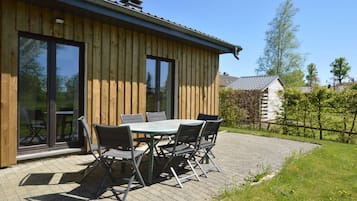 Guests can enjoy a patio with a table and chairs, surrounded by a grassy lawn and trees.