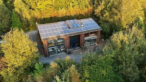Een modern huis met een dak van zonnepanelen, omgeven door dicht bos.