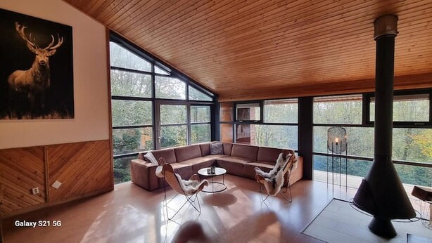Een ruime woonkamer met een grote hoekbank, een ronde salontafel en een open haard.