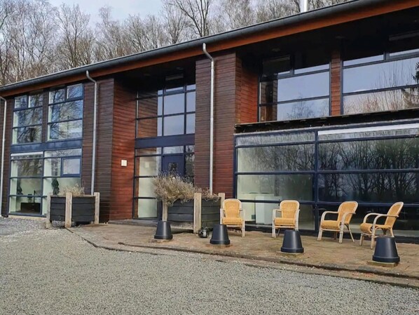 Een modern gebouw met grote ramen en een overdekt terras met stoelen en plantenbakken.