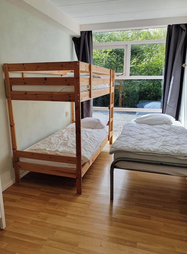 Een kamer met een stapelbed, een enkel bed en een raam met gordijnen.