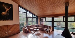 Een ruime woonkamer met een grote hoekbank, een ronde salontafel en een open haard.