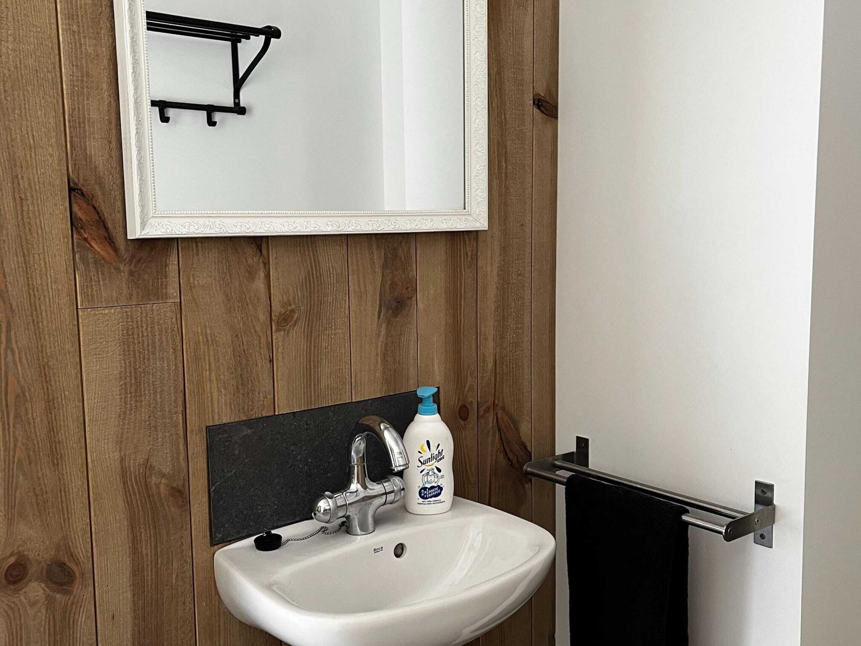 Ein Badezimmer mit einem weißen Waschbecken, einem Spiegel und einer Holzwand.