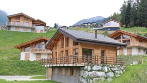 A wooden chalet with a balcony, set on a hillside with a view of other chalets and mountains. - Chalet in La Tzoumaz Near Ski Slopes (Riddes)