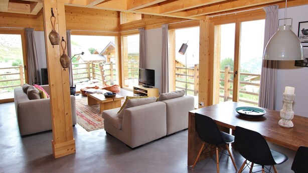 A spacious living area with a wooden ceiling, large windows, a sofa, a dining table with chairs, and a television. - Chalet in La Tzoumaz Near Ski Slopes (Riddes)