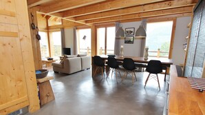 A spacious living area with a wooden ceiling, a sofa, a dining table with chairs, and large windows offering a view. - Chalet in La Tzoumaz Near Ski Slopes (Riddes)