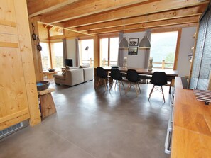 A spacious living area with a wooden ceiling, a sofa, a dining table with chairs, and large windows offering a view. - Chalet in La Tzoumaz Near Ski Slopes (Riddes)