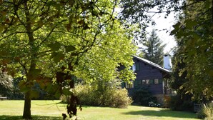 Un chalet rustique, doté de fondations en pierre, entouré d’une pelouse bien entretenue et d’un feuillage dense.