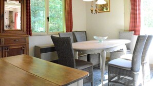 Un coin repas avec une table en bois et des chaises en osier, un luminaire suspendu et une fenêtre avec des rideaux.