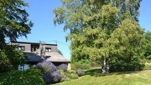A house with a sloped roof, surrounded by a well-maintained lawn and various shrubs. - Cozy Villa in Vielsalm With Private Garden (Vielsalm)