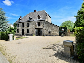 Un bâtiment en pierre avec une allée de gravier et une entrée fermée par un portail.
