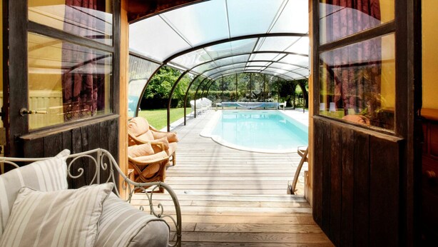 A covered outdoor area with a pool, wooden deck, and a bed with striped pillows. - Magnificent Holiday Home in Baronville With Heated Pool & Billiards (Beauraing)