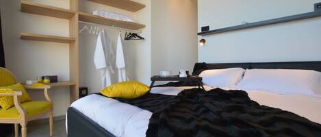 Una habitación de hotel con una cama, una silla, un escritorio y estanterías con ropa y una lámpara.
