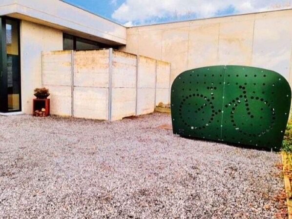 Un edificio moderno con patio de grava, una estructura verde con diseños circulares y una planta pequeña en maceta.