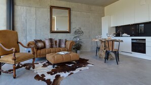 A modern living room with a leather sofa, a wooden armchair, and a dining table with a natural wood top. - Modern Villa Stay in Dalhem (Dalhem)