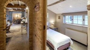 A room with a stone archway leading to a dining area, a bed with a white bedspread, and a window with a view of greenery. - Aesthetic Coastal Villa in Koksijde (Koksijde)