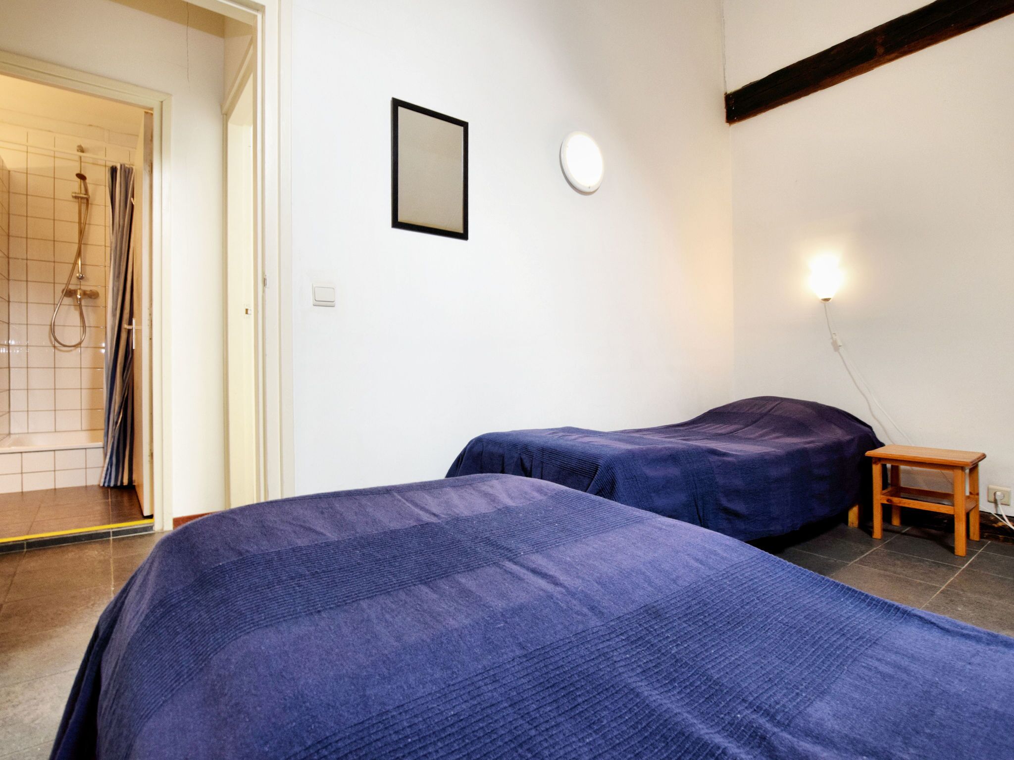 A room with two beds, a shower, and a small wooden table.