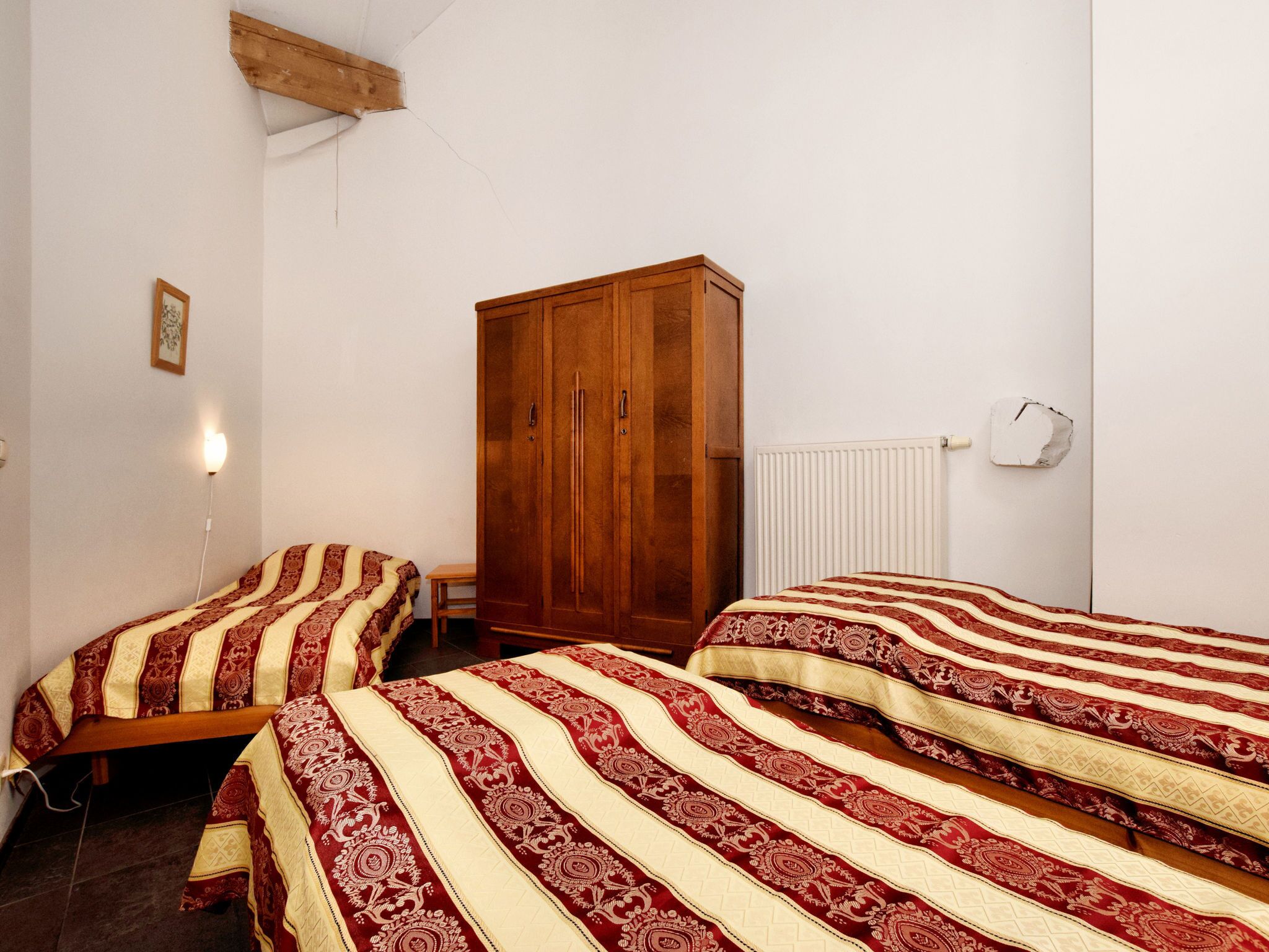 A bedroom with two beds, a wooden wardrobe, a radiator, and a small table.