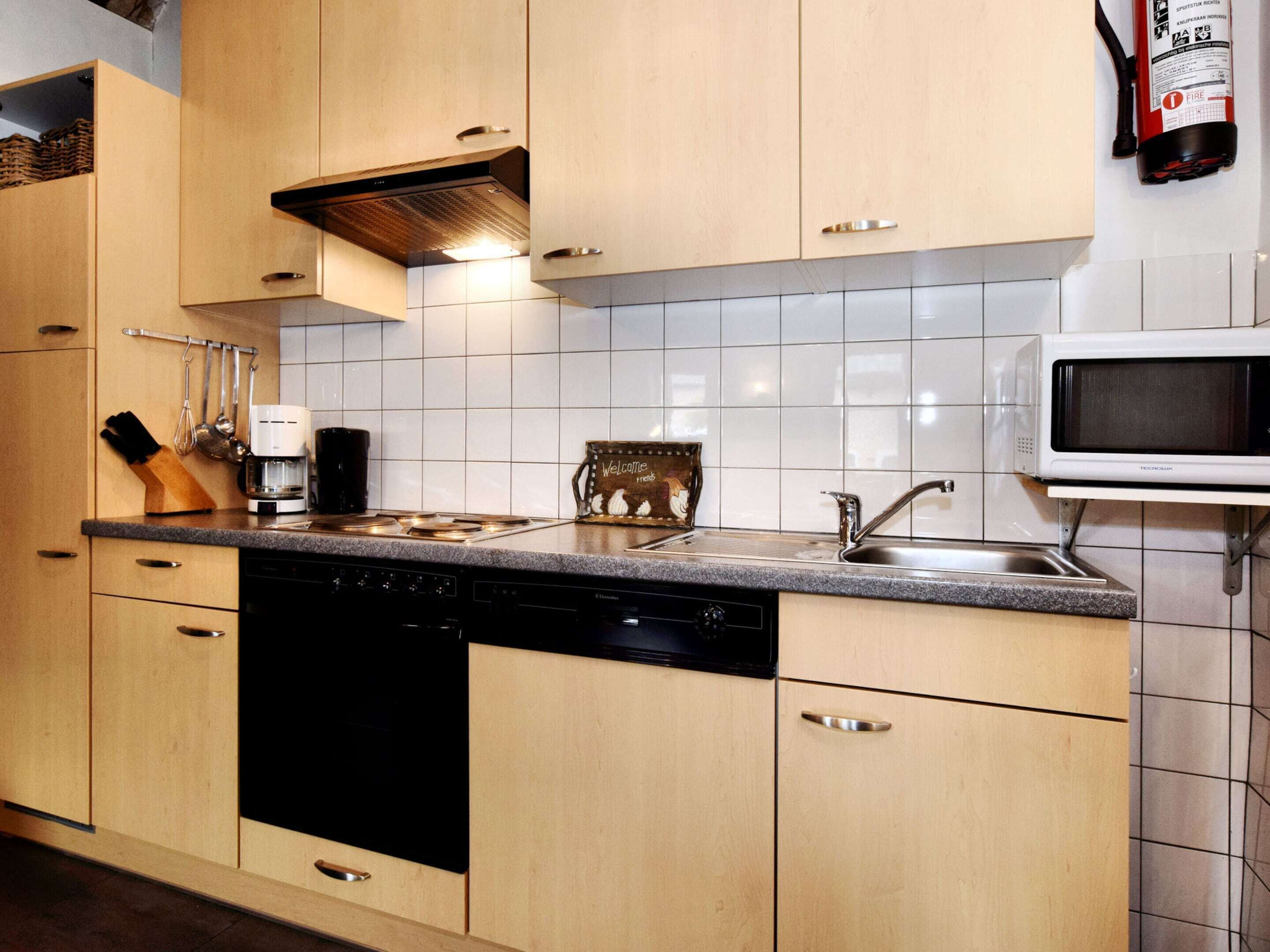 A kitchen with wooden cabinets, a dishwasher, a coffee maker, a microwave, and a fire extinguisher.