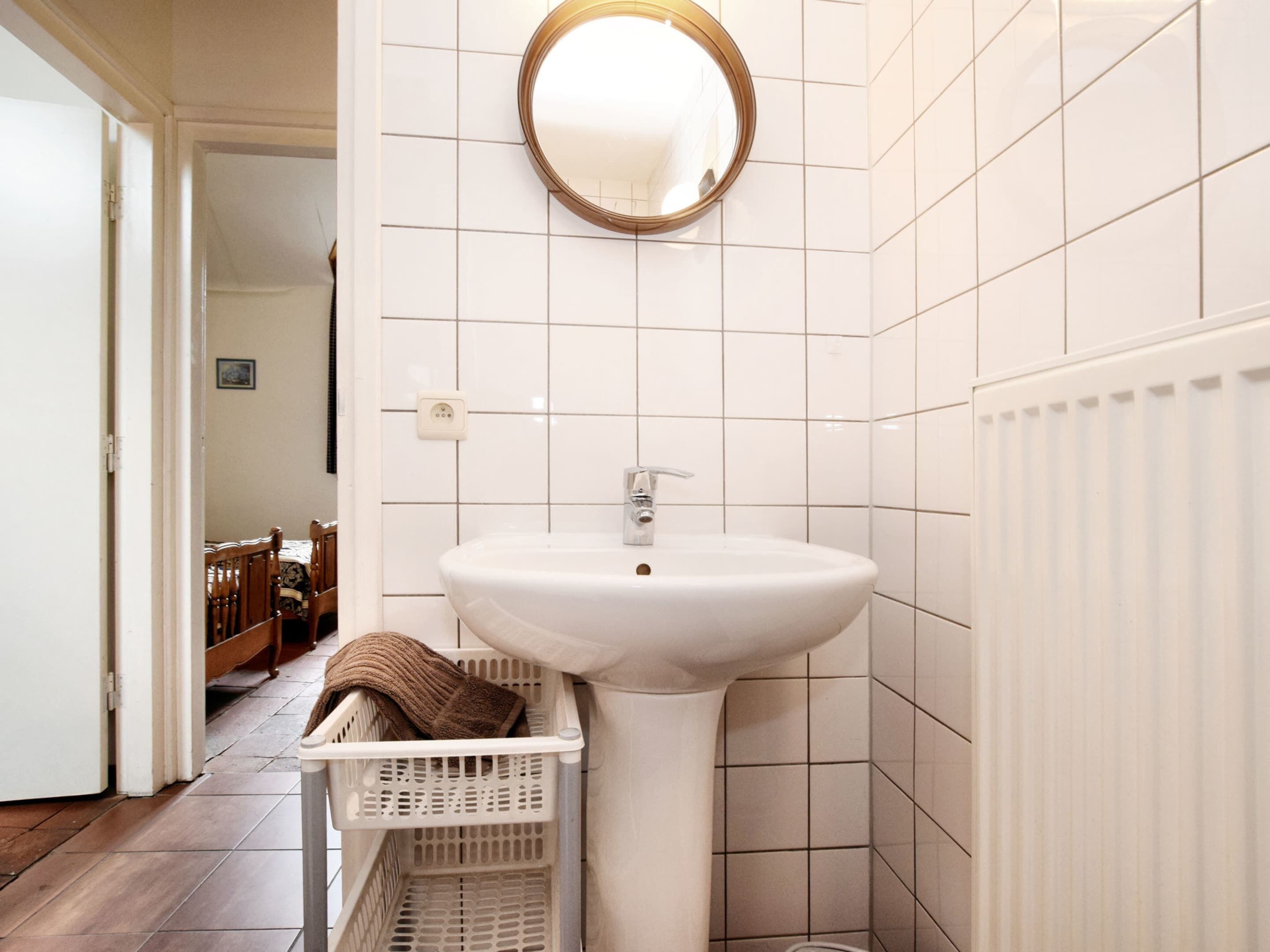A bathroom with a white sink, a mirror, and a towel basket.