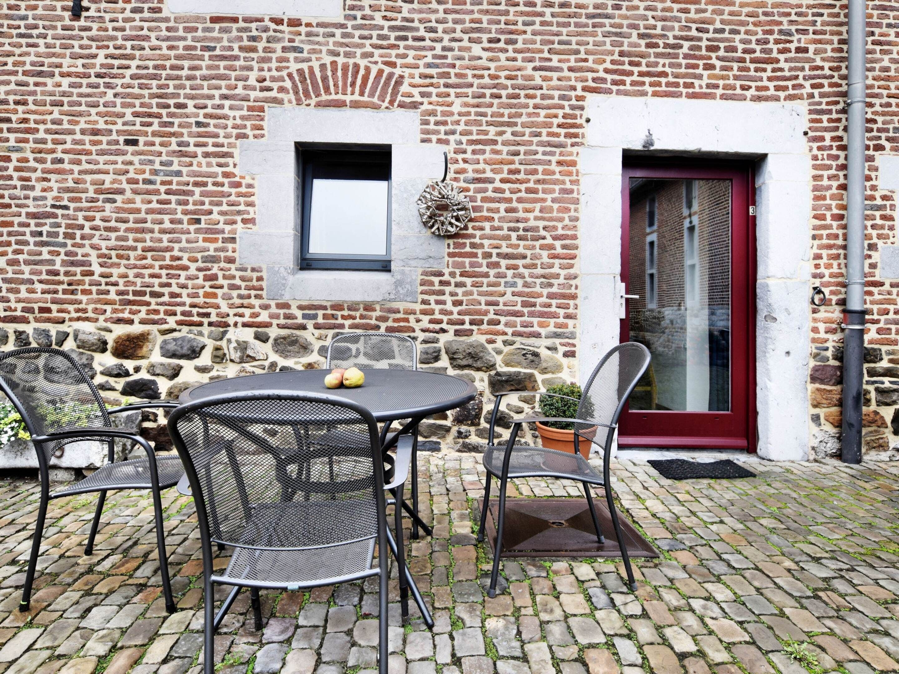 Ein Backsteinhaus mit roter Tür, einem Fenster und einem Tisch mit Stühlen davor.