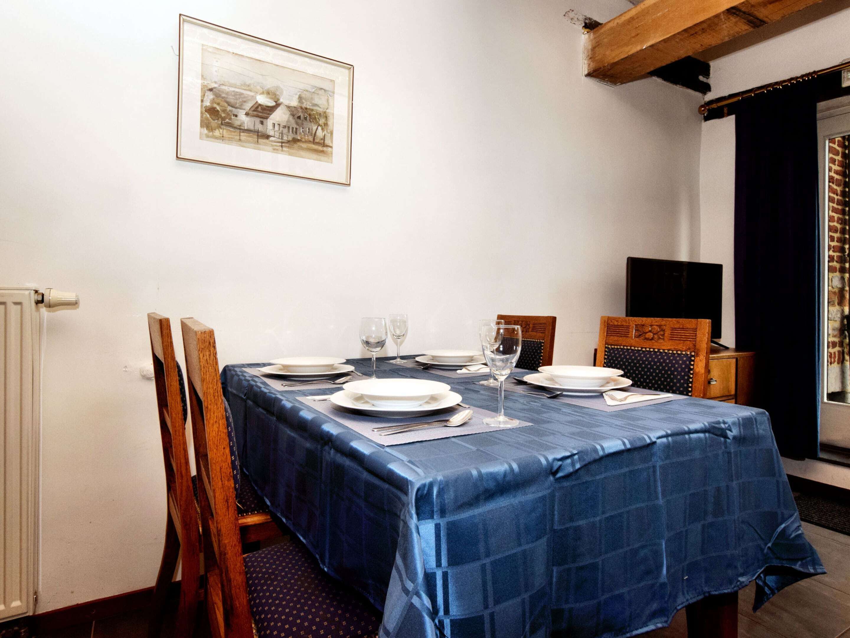 A dining room with a table set for four, a framed picture on the wall, and a window with curtains.