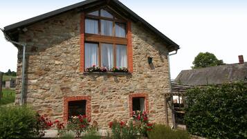 Un edificio de piedra con dos ventanas, una puerta de madera y un jardín con flores rojas.