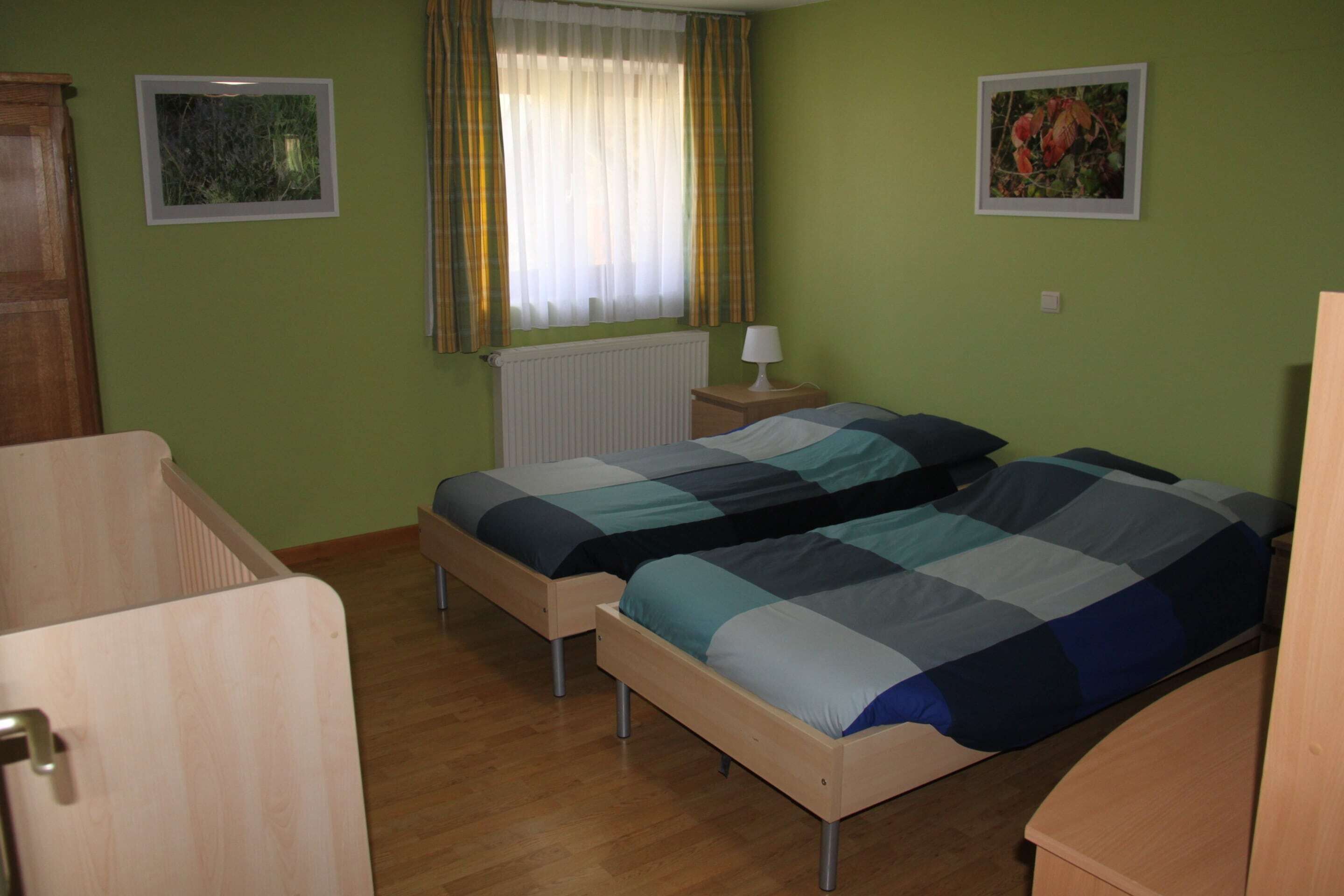 Une chambre avec deux lits simples, une fenêtre avec des rideaux, un radiateur et une petite table de chevet avec une lampe.