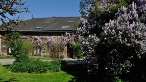 A stone building with a sloped roof and skylights, surrounded by lush greenery and blooming trees. - Lovely Holiday Home In Frahan With Terrace (Bouillon)