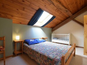 A cozy attic bedroom with a sloped ceiling, a skylight, a wooden bed, a nightstand, a small table, and a crib. - Lovely Holiday Home In Frahan With Terrace (Bouillon)