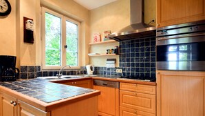 Una cocina con gabinetes de madera, salpicadero de baldosas negras, extractor de acero inoxidable y lavavajillas integrado.