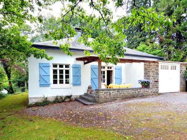 A quaint cottage with a stone foundation, a small porch with yellow chairs, and a white door.