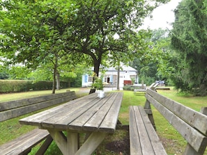 A wooden picnic table in a park with a house in the background.