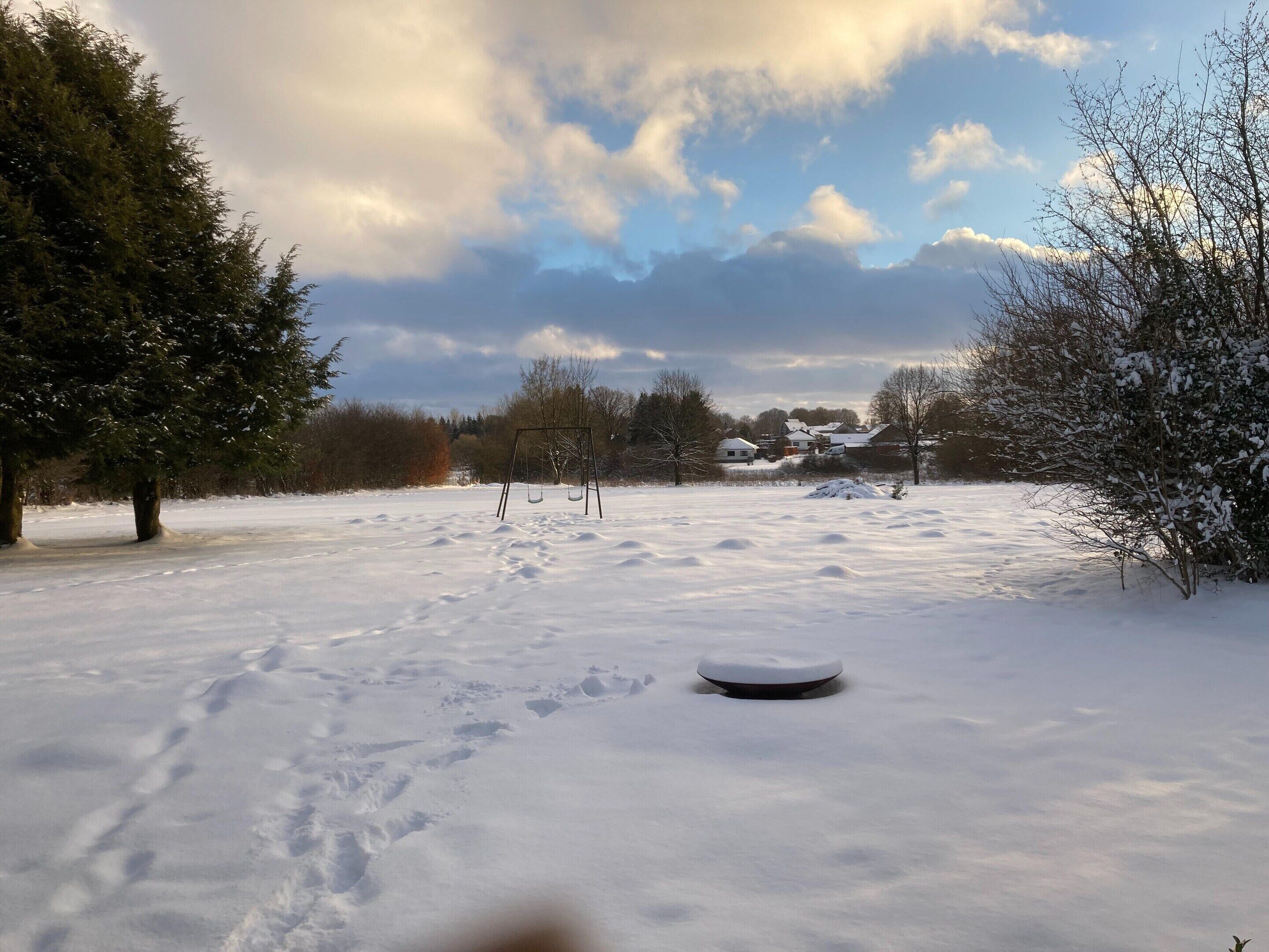 A snow-covered field with a swing set and a snow-covered bush.