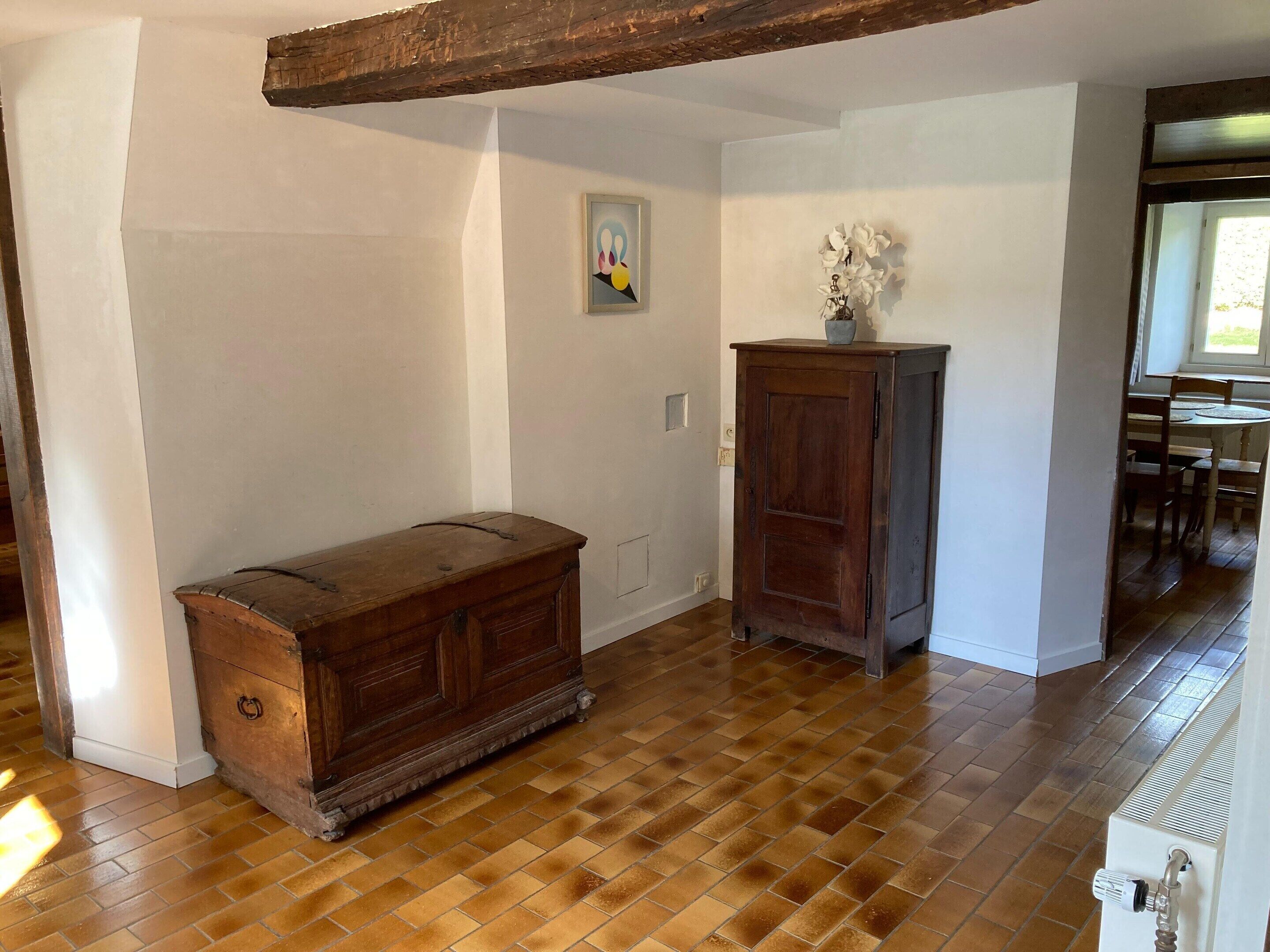 A room with a wooden cabinet, a painting on the wall, and a window with a view.