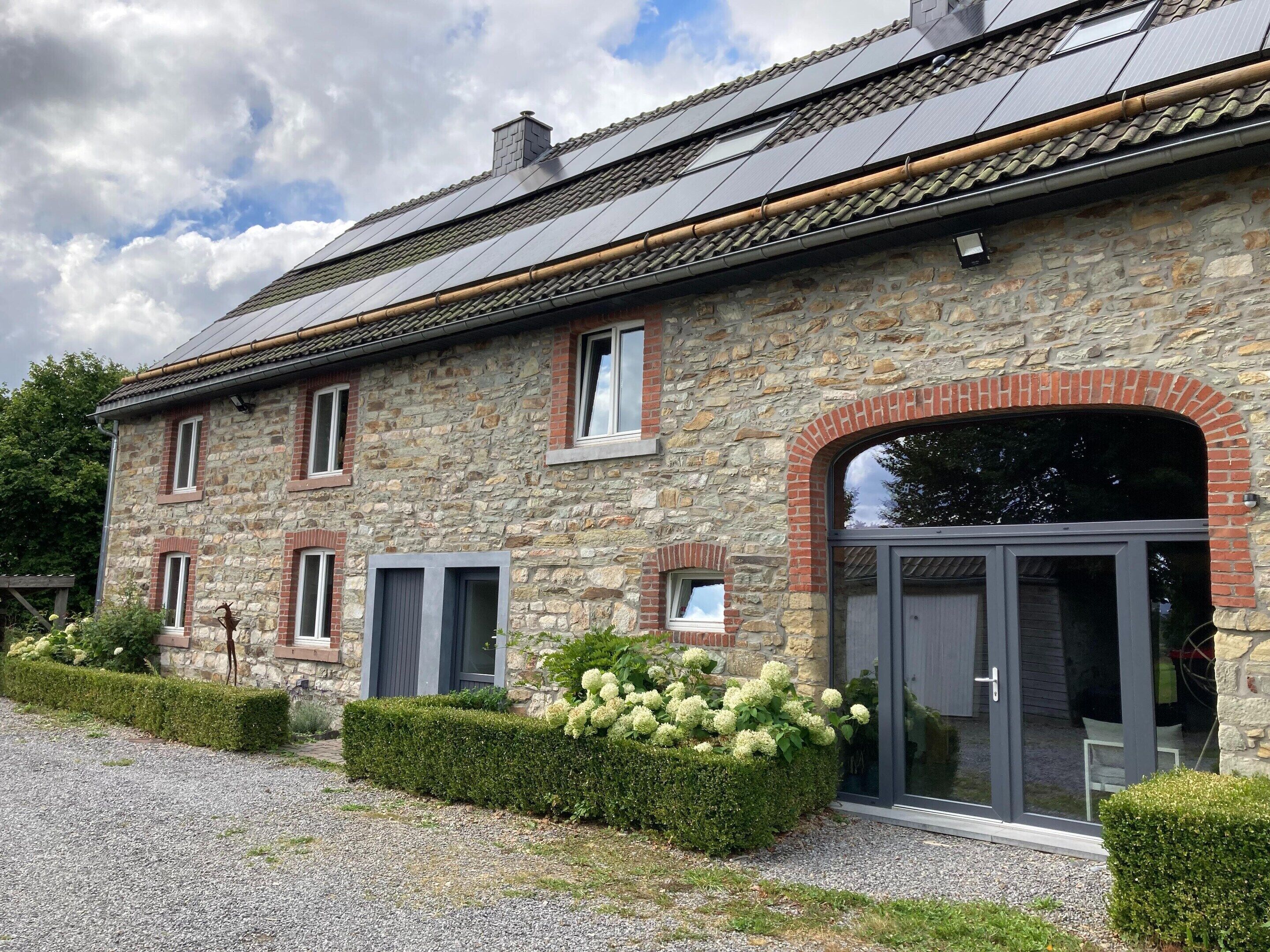 A stone building with a tiled roof, a large arched entrance, and a gravel driveway.