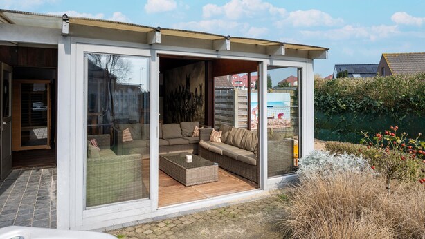 A modern house with a glass-enclosed porch, wicker furniture, and a view of the neighborhood. - Splendid Villa in Middelkerke with Sauna, Hot Tub, Terrace (Middelkerke)