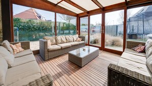 A sunroom with a wooden floor, a sofa, and a table. - Splendid Villa in Middelkerke with Sauna, Hot Tub, Terrace (Middelkerke)