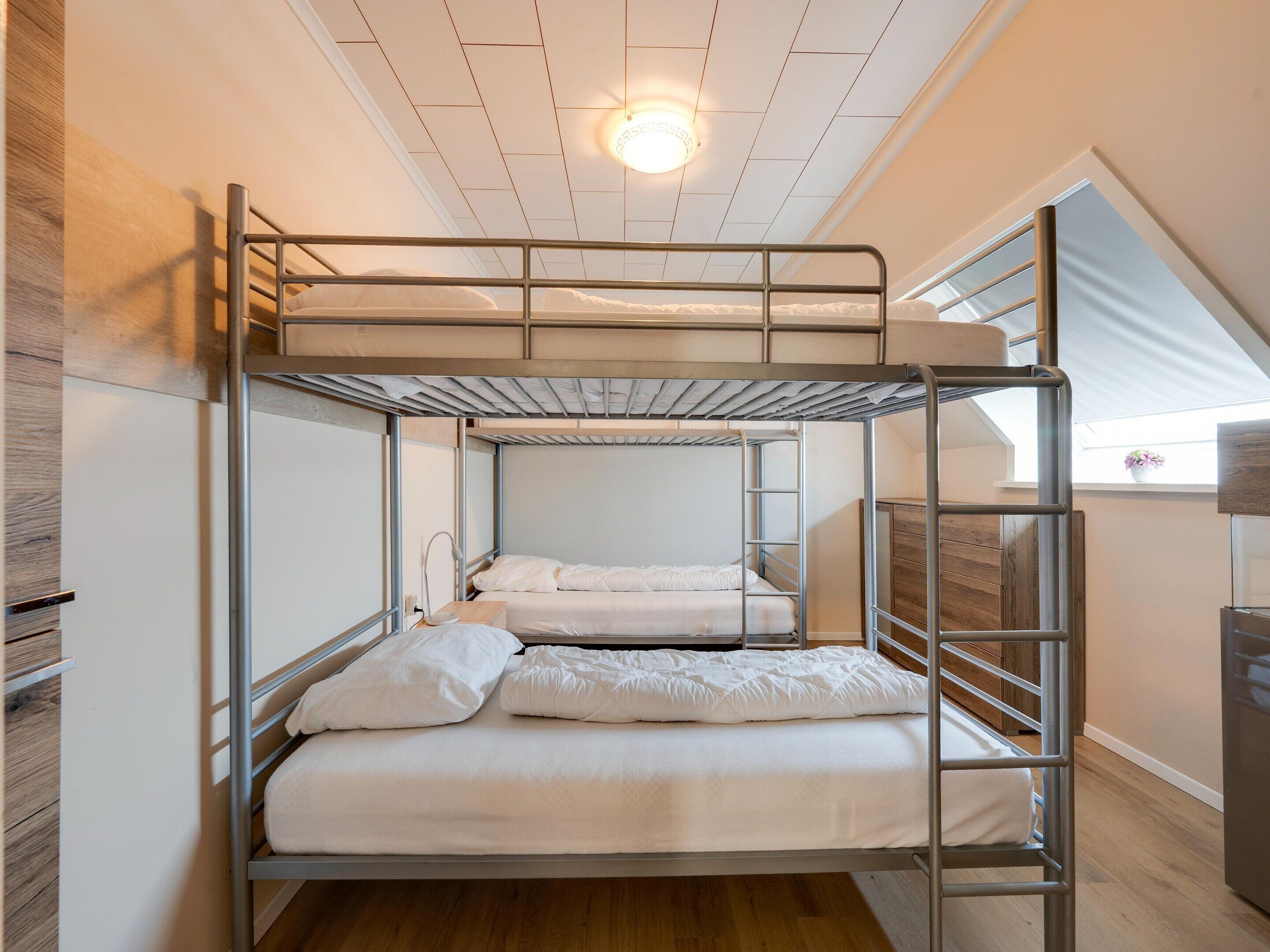 A bunk bed room with a skylight, wooden flooring, and a small desk with a lamp.