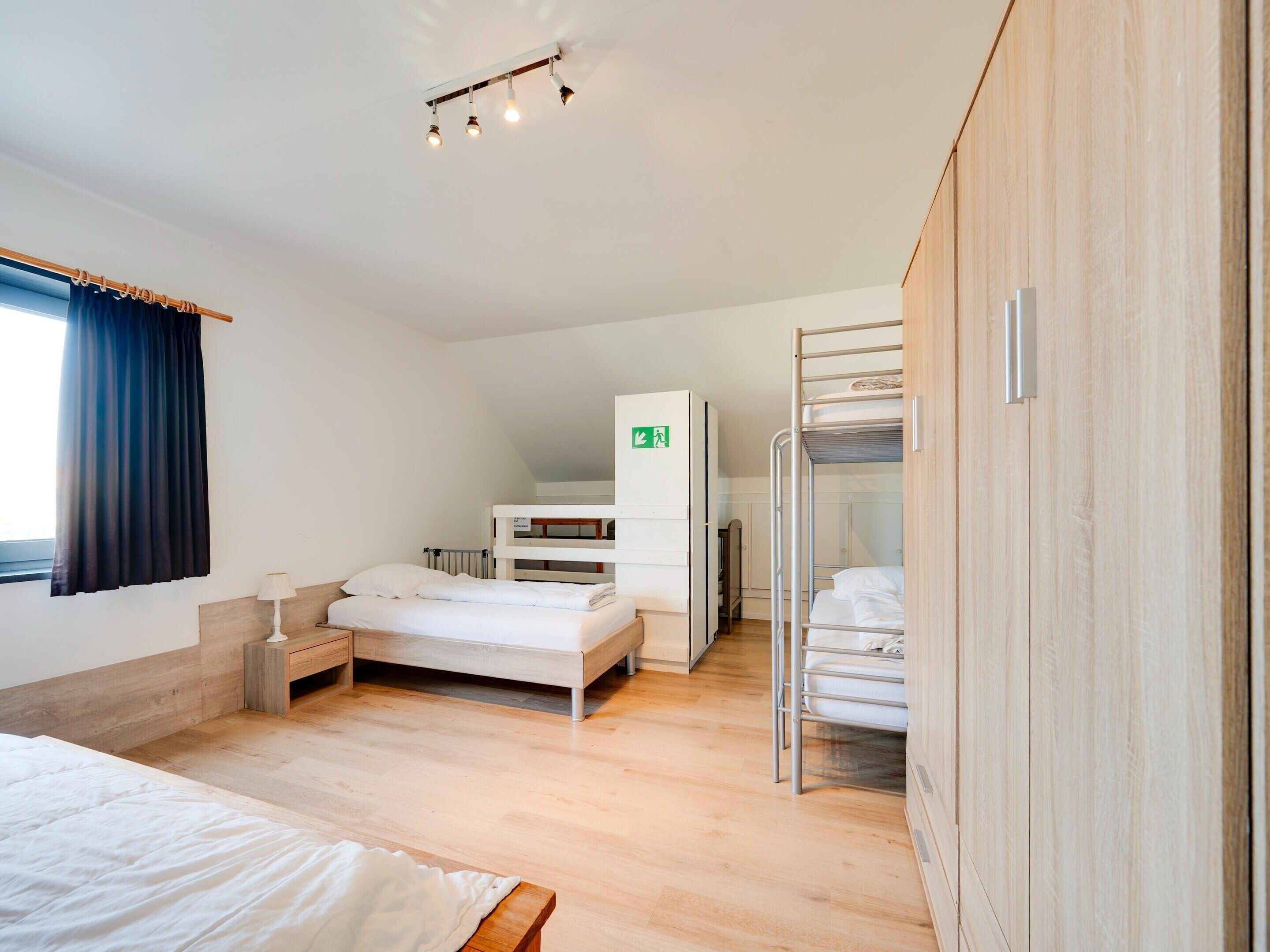 A room with a bunk bed, a desk with a chair, a radiator, and a window with curtains.