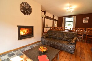 A living room with a fireplace, a leather sofa, a dining area with wooden chairs, and a clock on the wall.