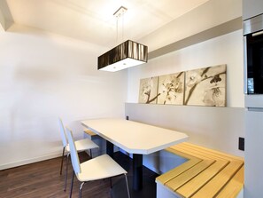 Ein moderner Essbereich mit einem weißen Tisch, vier weißen Stühlen, einer hölzernen Bank und einer hängenden Leuchte.
