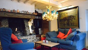 A cozy living room with a fireplace, blue sofas, a chandelier, and a large painting. - Holiday Home in Bievre Near Town Center (Bievre)