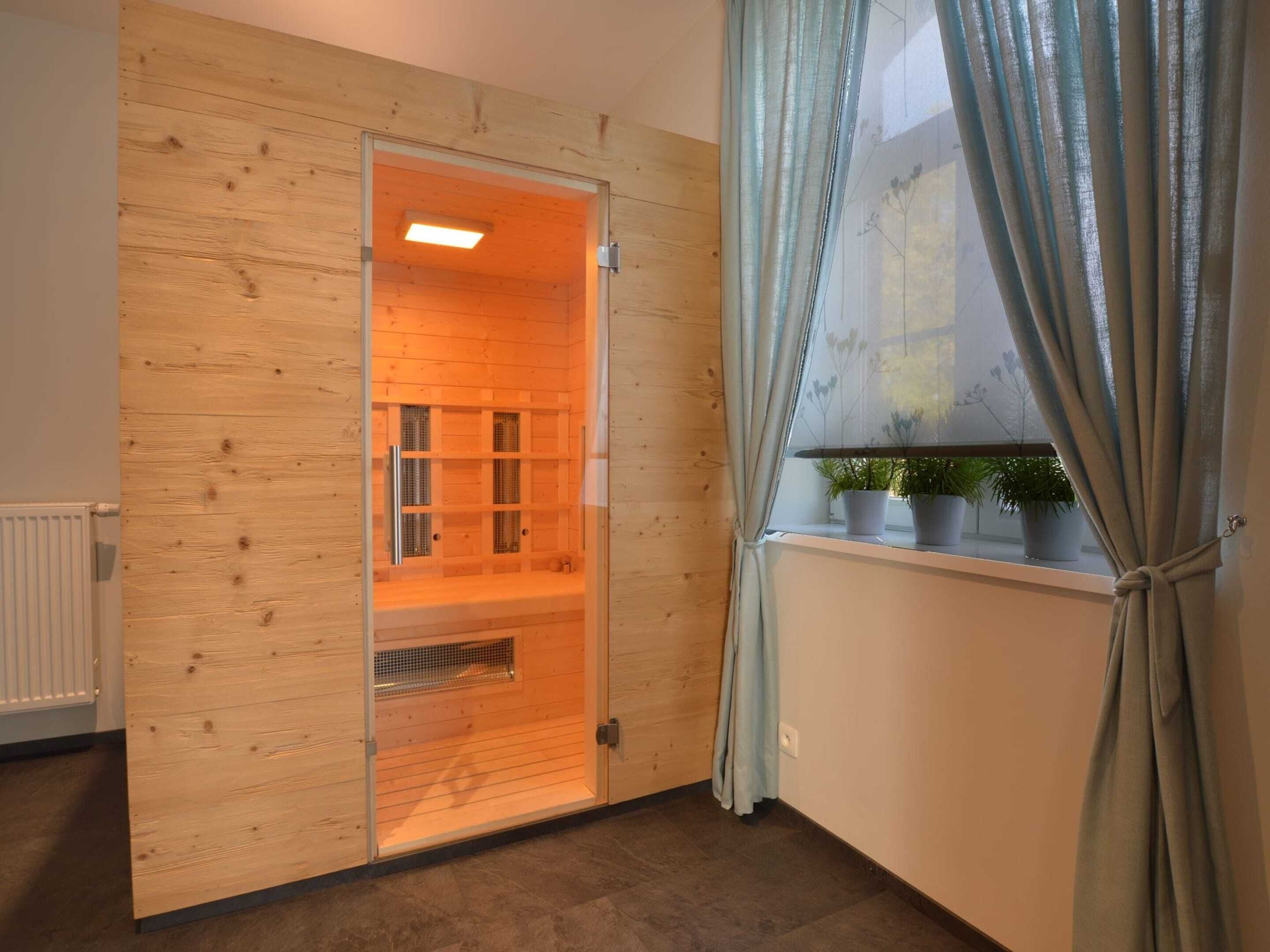 A sauna room with wooden walls, a glass door, and a window with curtains.