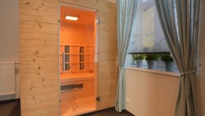 A sauna room with wooden walls, a glass door, and a window with curtains. - Charming Fens Family Home (Waimes)