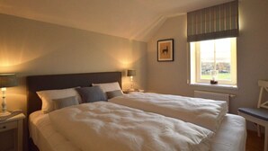 A hotel room with two beds, a window with a view, a framed picture on the wall, and a chair. - Charming Fens Family Home (Waimes)