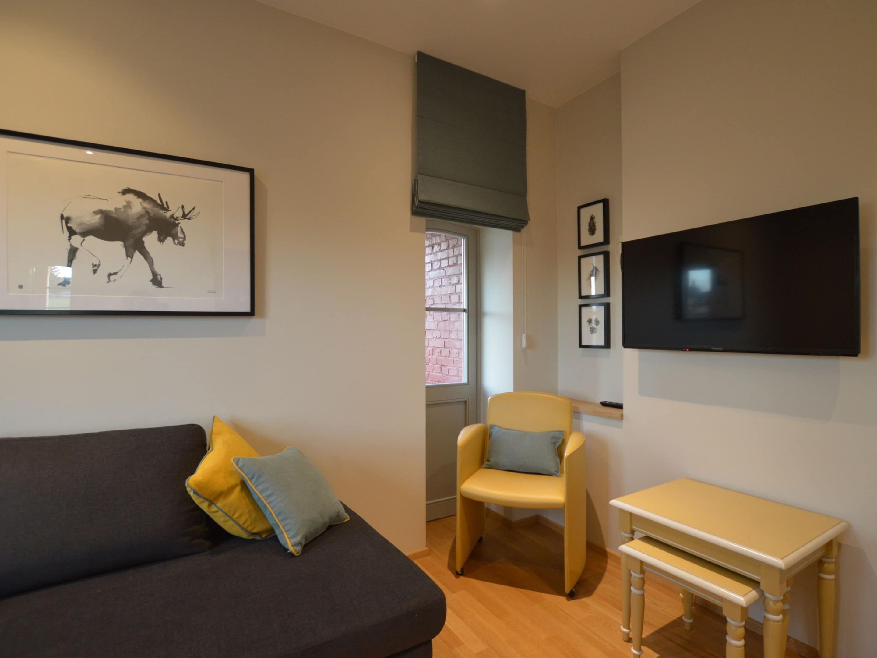 A modern living room with a dark sofa, a yellow armchair, a small wooden table, and a framed artwork of a horse.