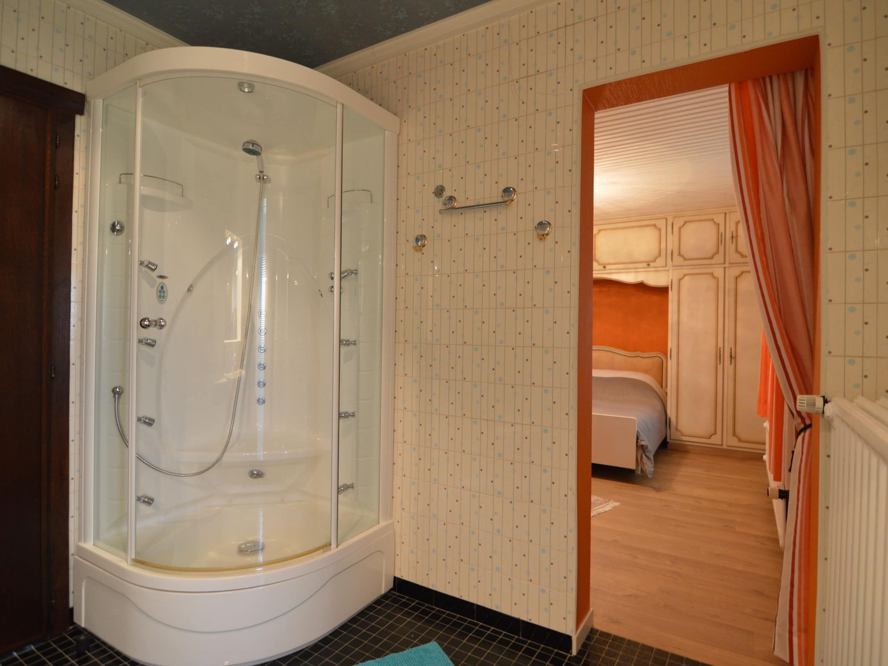 A bathroom with a glass-enclosed shower, a bed, and a tiled wall with a grid pattern.