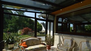 A sunlit patio with wicker furniture and potted plants, overlooking a garden and a house. - Elegant Villa in Stavelot With Fitness and Playroom and an Incredible Garden (Stavelot)